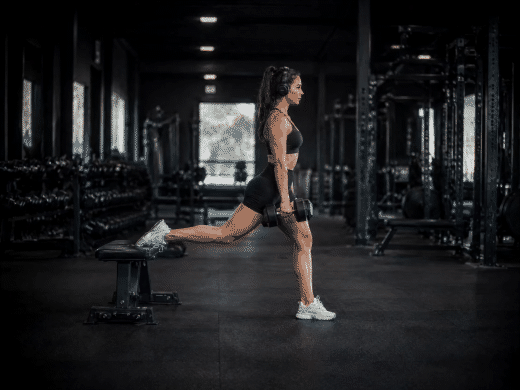 Frau mit Kopfhörern macht konzentriert Bulgarian Split Squats im Gym