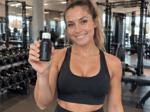 Frau im Gym hält den onors Performance Shot in die Kamera, dreht ihn auf und trinkt ihn in einem Zug