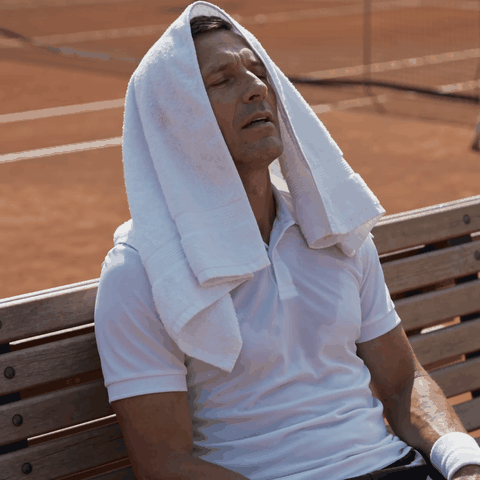 Tennisspieler sitzt komplett erschöpft mit Handtuch über dem Kopf auf der Court-Bank